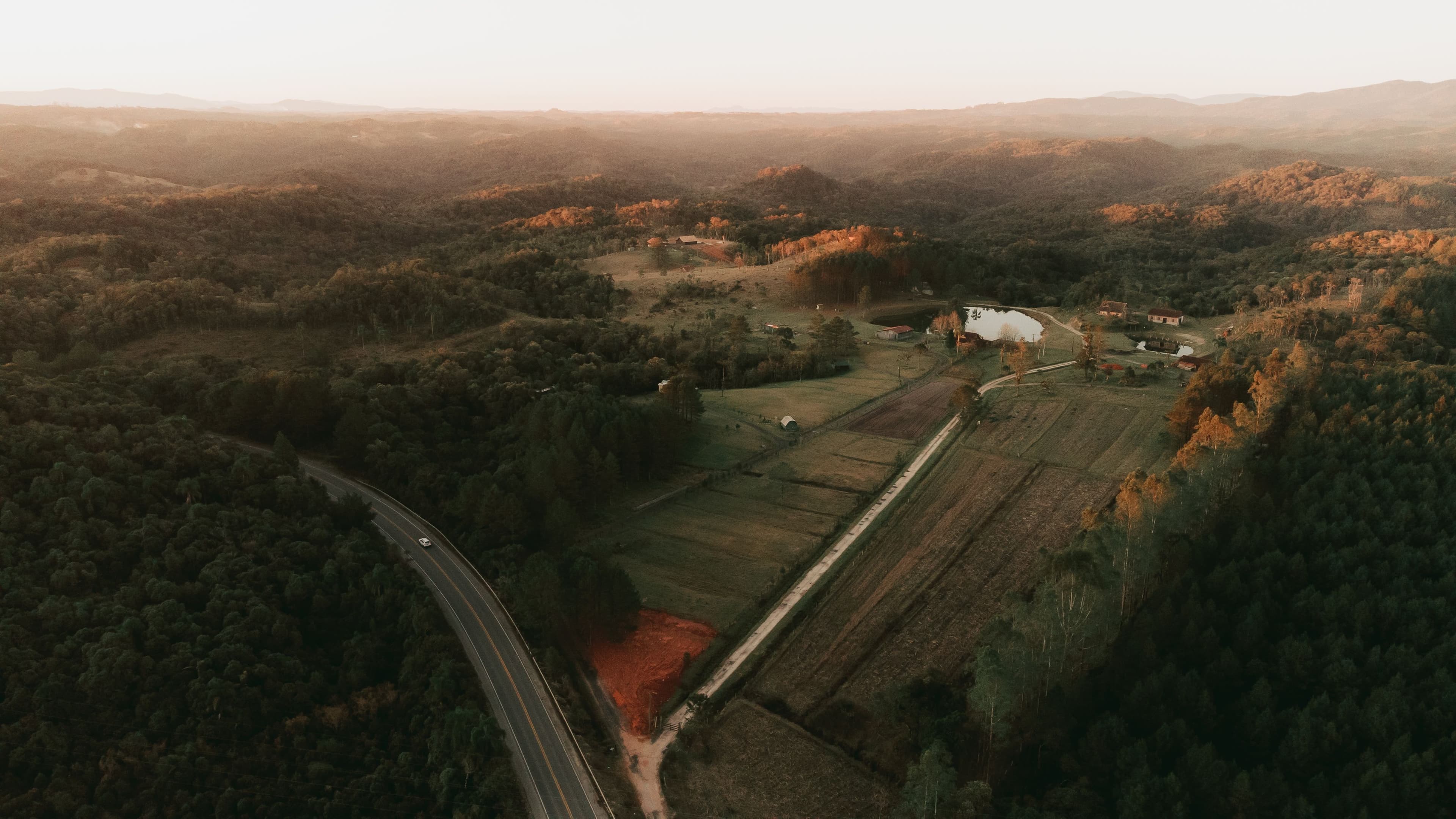 Aerial view of rural valley farmland, woodland and a winding road.