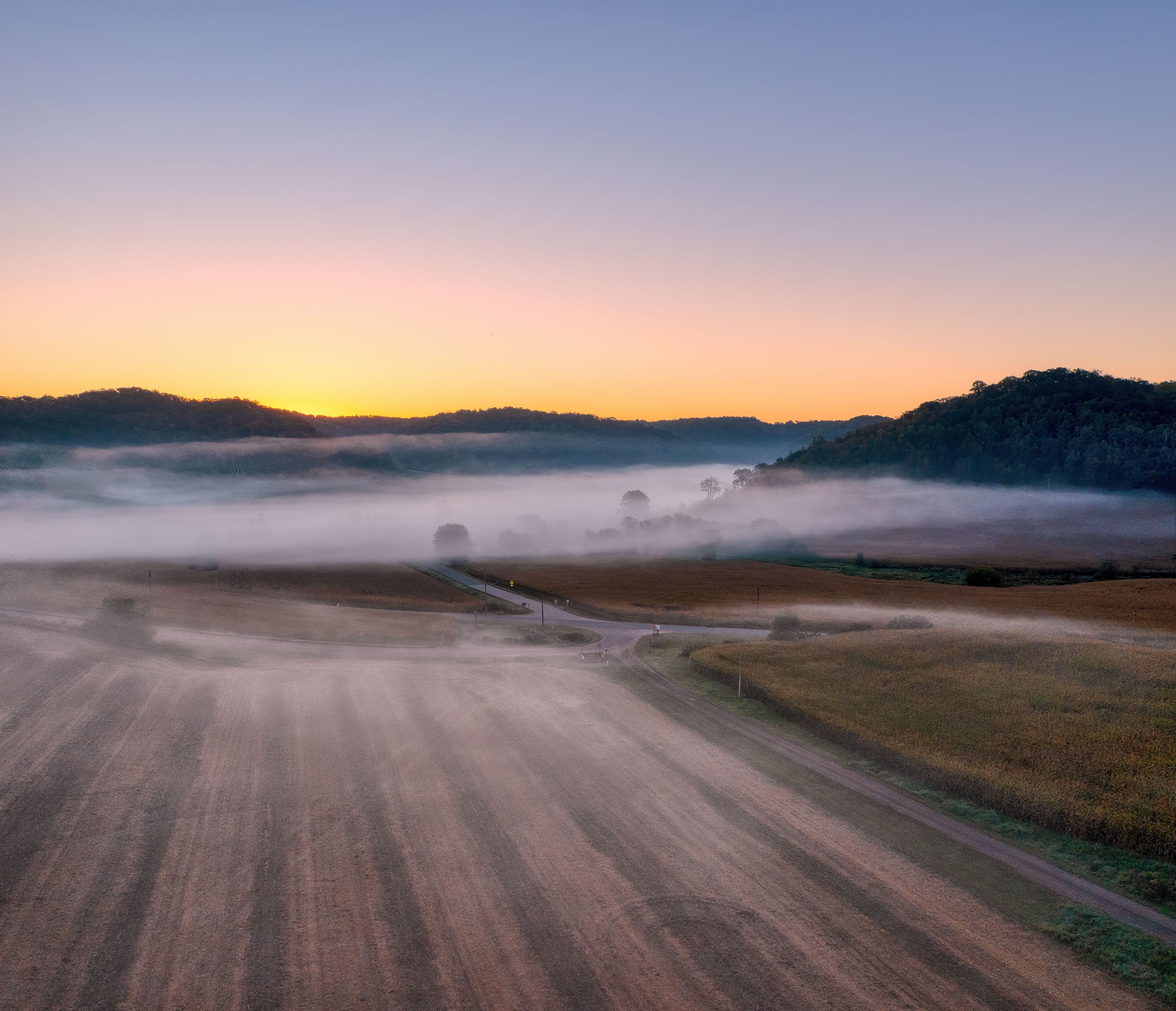 Misty rural farmland and a track at sunrise.
