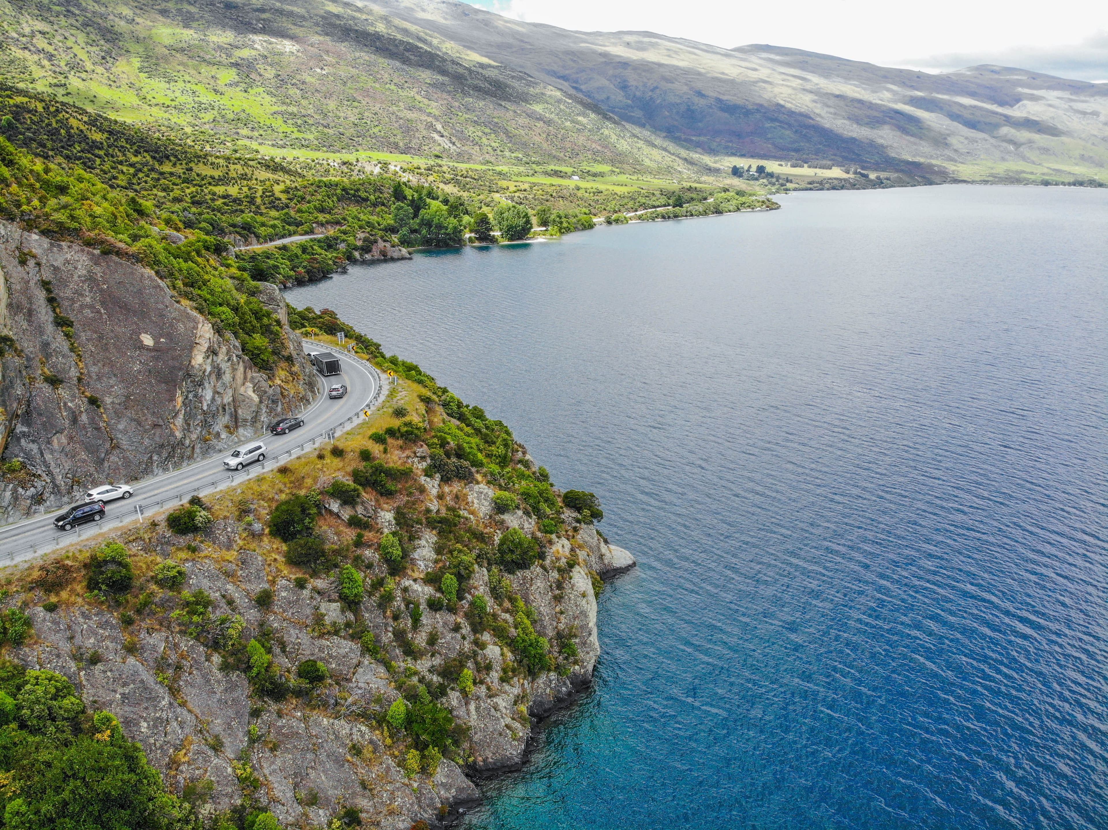 Aerial photograph of a rural road beside a lake and forested hills.